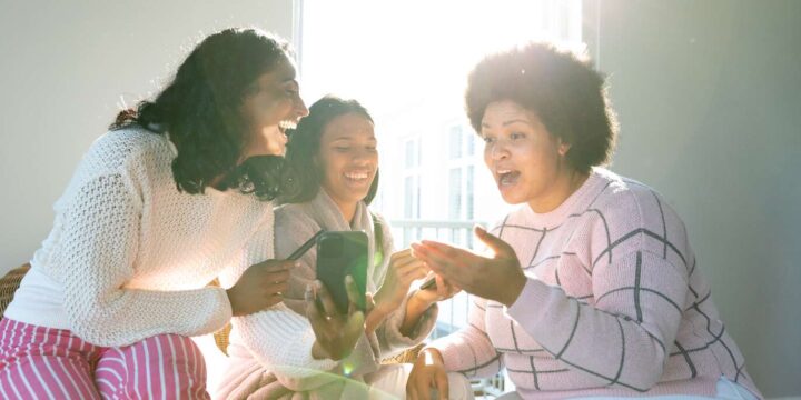 Tre kvinnor kollar på en mobiltelefon och ser upprymda ut