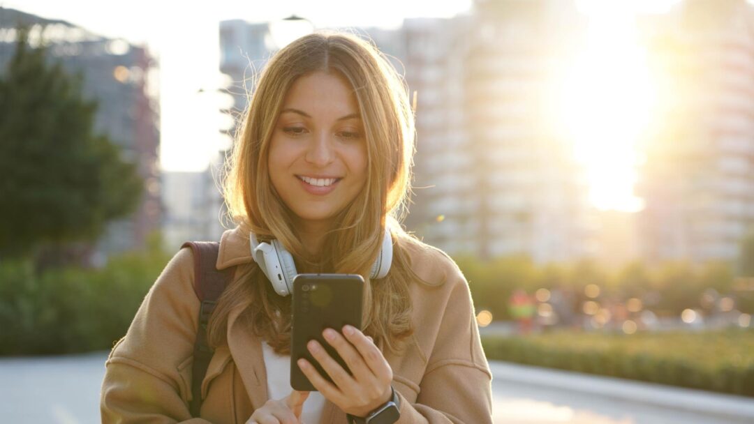 En kvinna kollar på en iphone och ser glad ut i solnedgången